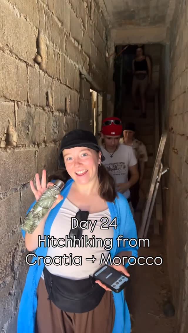 Grinning into the camera in a narrow stone stairwell, a patterned bottle held up, three others coming down the steps behind.