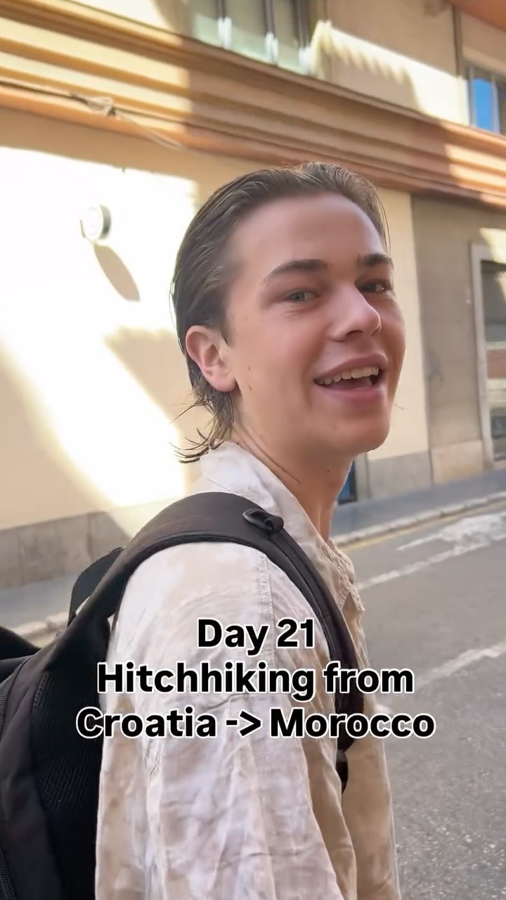 Turning back towards the camera on a sunlit street, backpack on, twenty-one days in.